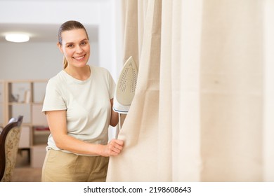 Young Woman Ironing Curtains At Home