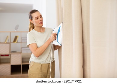 Young Woman Ironing Curtains At Home