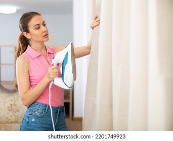 Young Woman Ironing Curtains At Home