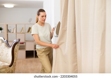 Young Woman Ironing Curtains At Home