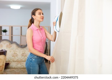 Young Woman Ironing Curtains At Home