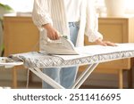 Young woman ironing towel on board in laundry room, closeup