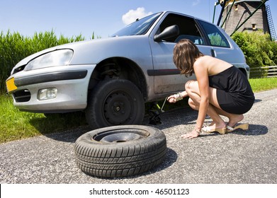 Young Woman Jacking Up Her Car To Change A Flat Tire With A Spare One