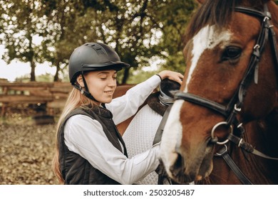 A young woman jockey adjusts the harness on her horse before training. Preparing for an equestrian competition. - Powered by Shutterstock