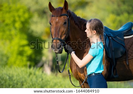 Young woman jockey with brown horse walking across field.