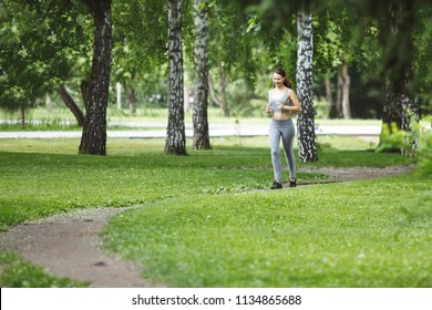 Young Woman Jogging Down A Path In A Green Park.