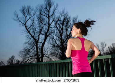 Young Woman Jogging At Night With The Tree In The Background. Girl Running Outdoors In A City Park. Color Toned Image.