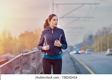 Young Woman Jogging On The Street Early In Morning. Fit And Healthy Brunette Girl Working Out During Winter In The City. Runner Work Out In An Urban Context On Bridge.