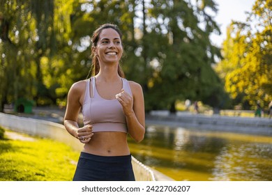 Young woman jogging outdoors. Concept of healthy lifestyle. Happy female runner jogging in the morning in nature. Sports training. Young woman running against morning sun - Powered by Shutterstock