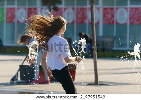Young woman jogging though the water of fountain in the Moscow public park. She is having fun . Hot summer amusement. Leisure, beauty and happiness concept. Frontal view
