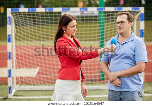 Young woman journalist interviews man near goal\
at stadium.