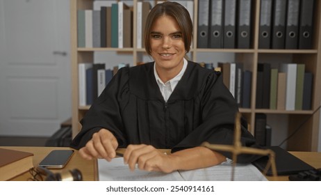 Young woman judge smiling in a courtroom dressed in a black robe with shelves of legal books in the background. - Powered by Shutterstock