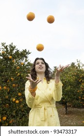 Young Woman Juggling Oranges In An Orange Grove.