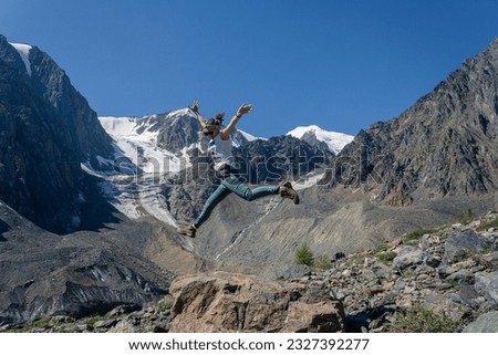 a young woman in a jump against the backdrop of the high mountains of Altai with snow-capped peaks and a glacier. Summer landscape Aktru.