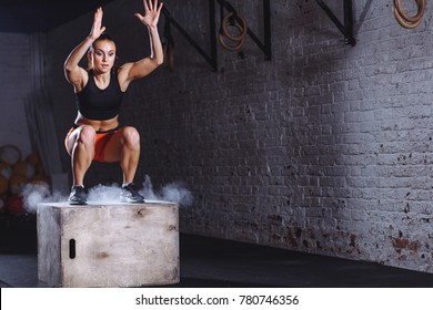 young woman jumping box and talc powder departs from under feet. Fitness woman doing box jump workout at cross fit gym.