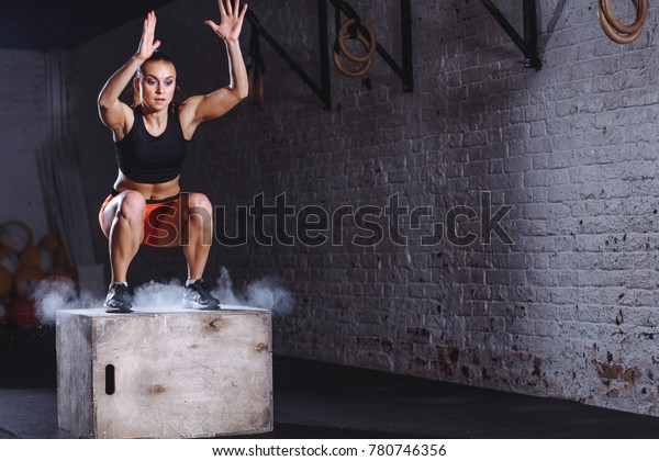 young\
woman jumping box and talc powder departs from under feet. Fitness\
woman doing box jump workout at cross fit\
gym.