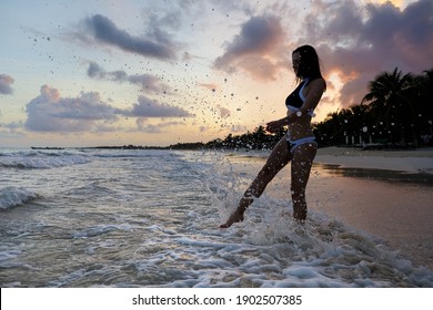 A Young Woman Jumping Into Water With Sunset Behind In Tulum Beach In Mexico