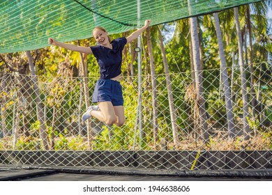 Young woman jumping on an outdoor trampoline, against the backdrop of palm trees