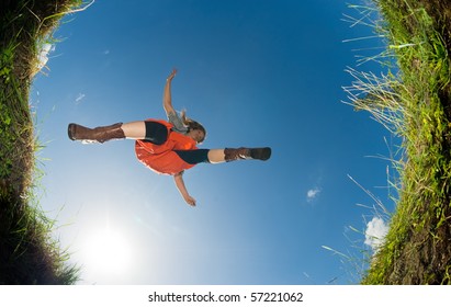 Young Woman Jumping Over A Creek; Shot From Below