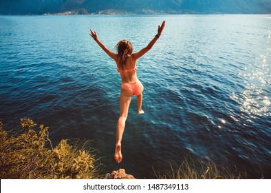 Young Woman Jumping From A Rock Into The Sea.