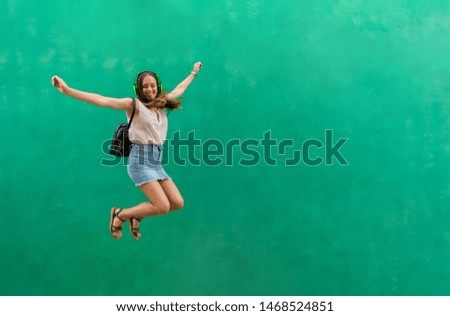 Young woman is jumping while she is listening music on green background. Lifestyle concept, fun.