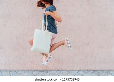 Young Woman Is Jumping With White Cotton Bag In Her Hands.