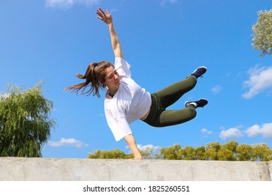 A young woman jumps over a wall on a sports street playground