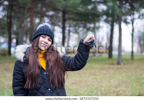 Young  woman just bought a new car. female
holding keys from new automobile. Female in dark clothes and and
cap is smiling.