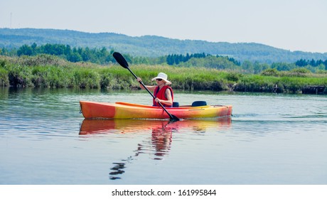 Young Woman Kayaking Alone on a Calm River and Wearing a Safety Vest - Powered by Shutterstock