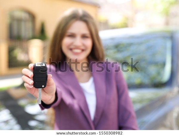 Young\
woman with key near new car outdoors, focus on\
hand