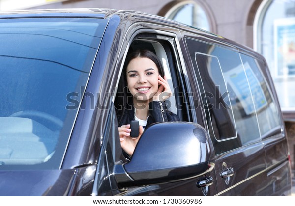 Young woman with key sitting in car outdoors. Buying\
new auto