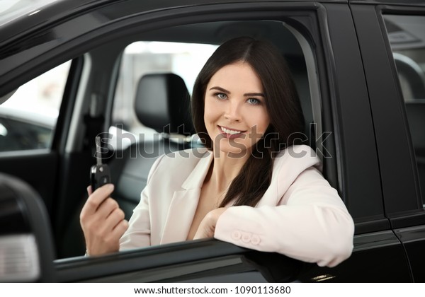 Young woman with key sitting in driver\'s seat of\
auto. Buying new car