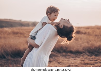 Young woman kisses her little son at sunny in the meadow in sunset. Young mother holding her baby. Mother and  little son having good time in the nature. Color toned image. Mothers Day. Family Concept