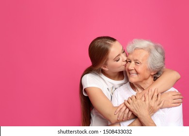 Young woman kissing her grandmother on pink background. Space for text - Powered by Shutterstock