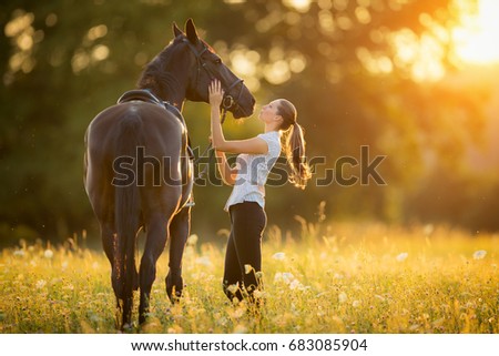 Young woman kissing horse in evening sunset light. Outdoor photography with fashion model girl. 