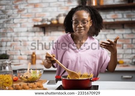 Young woman in kitchen. Beautiful African woman cooking pasta.