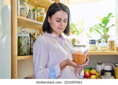 Young Woman In Kitchen With Containers Jars Of Food, Holding A Jar Of Red Lentils