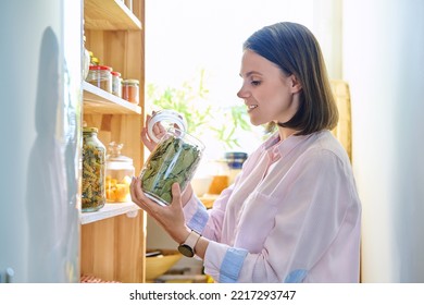 Young woman in kitchen with containers jars of food, holding jar of dry bay leaves