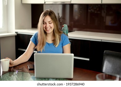 Young Woman In Kitchen During Quarantine. Stand Alone And Talk On Phone. Online Wireless Communication. Remote Home Work With Parrot.