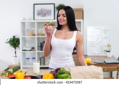 Young Woman In The Kitchen Having Healthy Breakfast, Eating Wholesome Sandwich With Vegetables And Glass Of Milk Front View Portrait