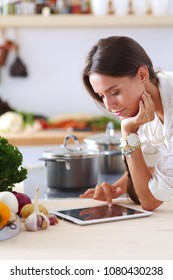 Young Woman In The Kitchen, Using Her Ipad. Young Woman