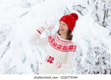 Young Woman In Knitted Sweater Playing Snow Ball Fight In Winter. Girl In Family Snow Balls Game. Female In Knit Handmade Hat And Mittens With Christmas Snowflake Design Having Fun In Snowy Park.