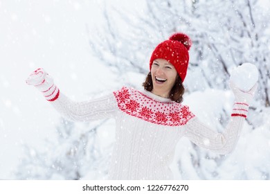 Young Woman In Knitted Sweater Playing Snow Ball Fight In Winter. Girl In Family Snow Balls Game. Female In Knit Handmade Hat And Mittens With Christmas Snowflake Design Having Fun In Snowy Park.