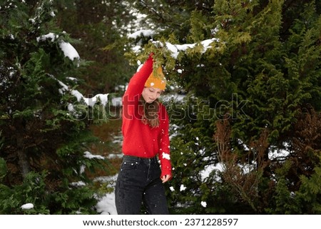 A young woman in a knitted sweater shakes snow from a green Christmas tree and has fun outdoors
