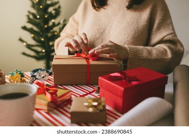 Young woman in knitted sweater wrapping Christmas presents using paper, scissors and colorful ribbons. Festive holiday preparations. - Powered by Shutterstock