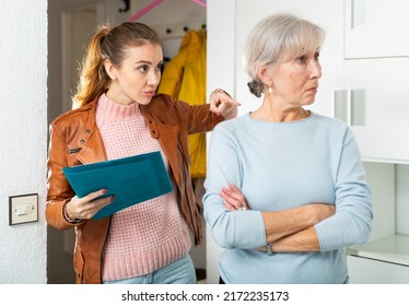 Young Woman Landlord Standing Near Senior Woman Tenant And Pointing With Finger On Problem In House. Senior Woman Standing With Folder Hands.