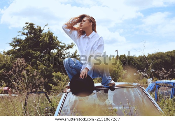 Young\
woman landscapes above the clouds, standing on the car. Carefree\
lifestyle. Young woman on car hood. Abandoned\
car.