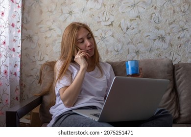 Young Woman With Laptop And Cup Of Tea Talking On The Phone At Home On The Couch. Freelancer, Blogger Concept