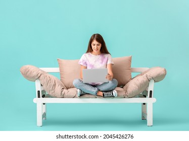 Young Woman With Laptop On Modern Sofa Against Color Background