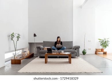 Young Woman With Laptop And Phone Telecommuting On The Sofa At Her Home